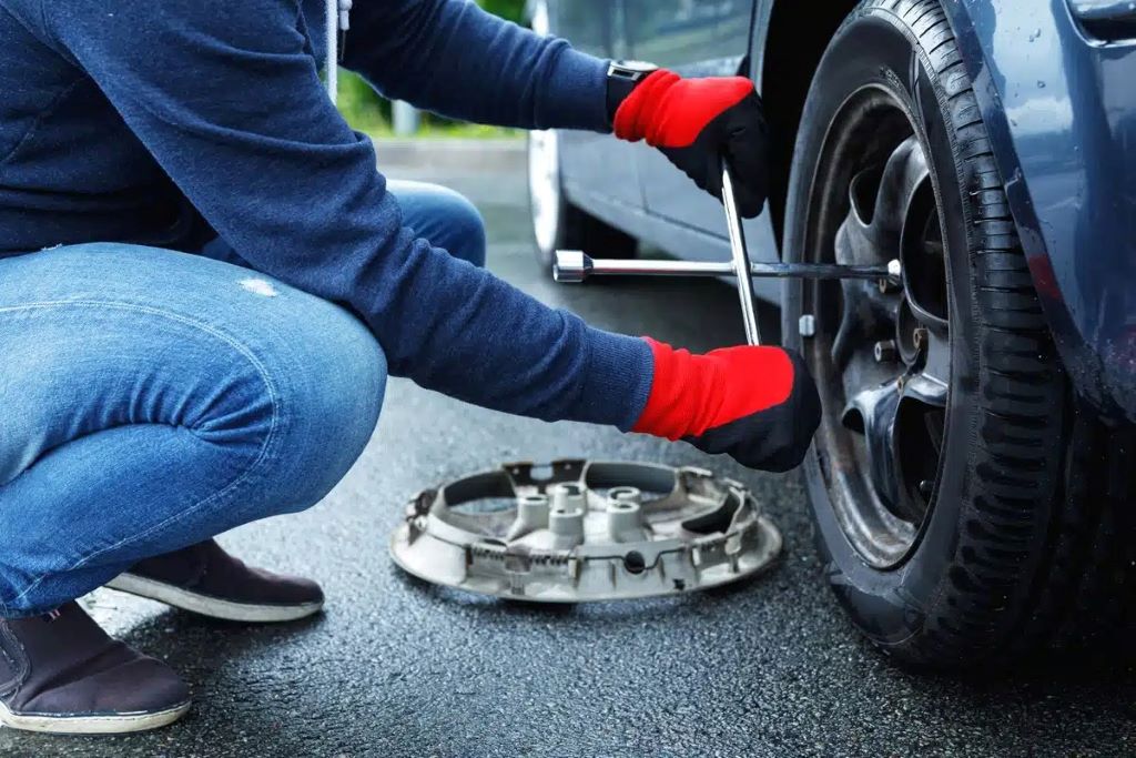 Close-up of hands removing a flat tire, showing tools and process for tire change guide