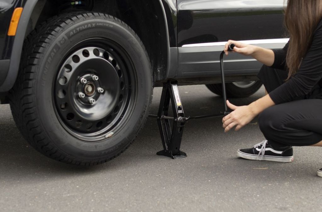 Driver changing a car tire with a jack and wrench, illustrating step-by-step tire replacement