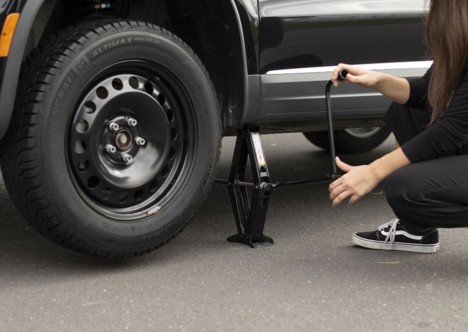 Driver changing a car tire with a jack and wrench, illustrating step-by-step tire replacement