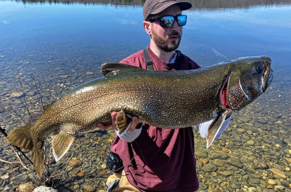 Angler holding large lake trout caught in small freshwater lake with fishing rod and reel