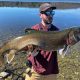 Angler holding large lake trout caught in small freshwater lake with fishing rod and reel