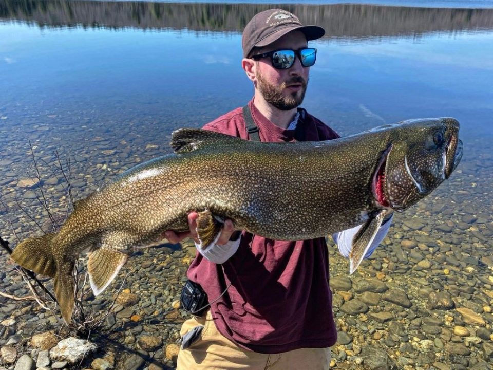 Angler holding large lake trout caught in small freshwater lake with fishing rod and reel