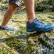 Close-up of blue aqua shoes stepping onto slippery limestone in a shallow river.