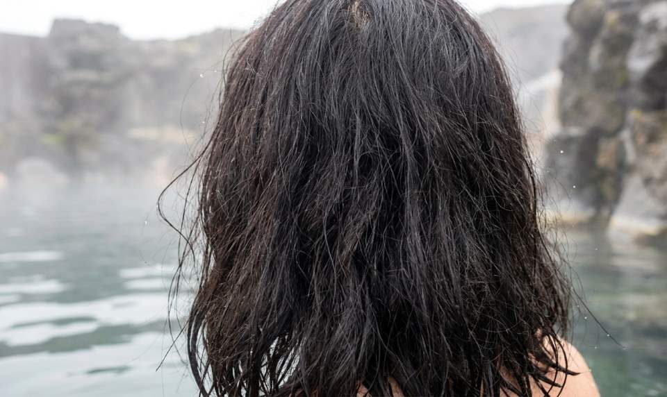 Person applying a deep conditioning mask to dry hair after a thermal mineral spa soak